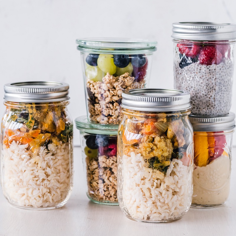 Stacked mason jars of meal prep: rice with roasted vegetables, granola with fruit, and berry chia pudding