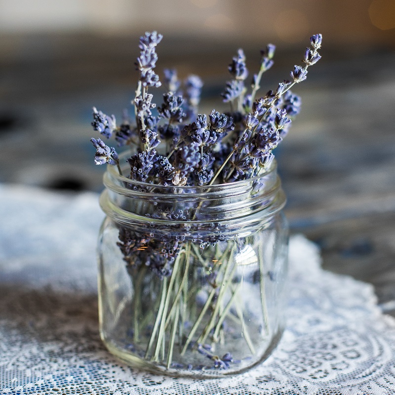 A bunch of dried lavender in a small mason jar vase on a lace doily